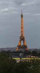 Eiffel Tower glows golden against cloudy Paris evening sky