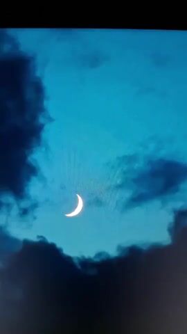 A crescent moon is visible in a deep blue sky filled with dark, wispy clouds. The moon is illuminated and appears bright against the dark clouds.