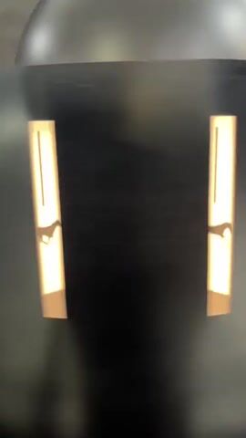 The video shows a dark, cylindrical object with two vertical, illuminated rectangular slits. Shadows of small figures are visible within the slits, appearing to move. The figures are silhouettes, with indistinct features, but some appear to have limbs. The lighting is bright yellow, and the background is dark.