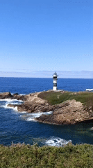Striped lighthouse on rocky Galician coast, clear summer day