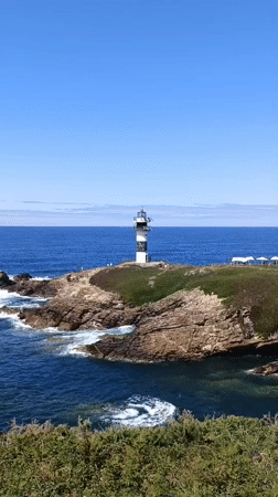 Striped lighthouse on rocky Galician coast, clear summer day