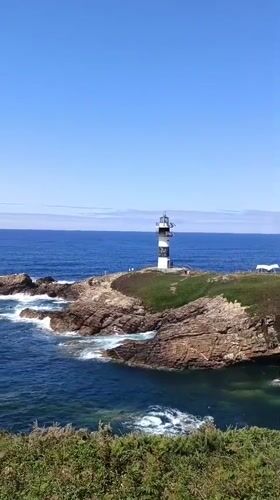 Striped lighthouse on rocky Galician coast, clear summer day