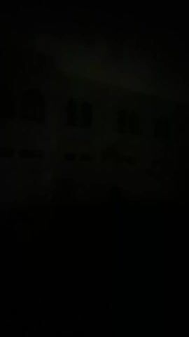 The video shows a two-story building at night, or in very low light. The building has arched windows on the second floor. The overall scene is dark, and the video quality is poor, but the building's silhouette is discernible. Light levels fluctuate, making the building appear and disappear from view.