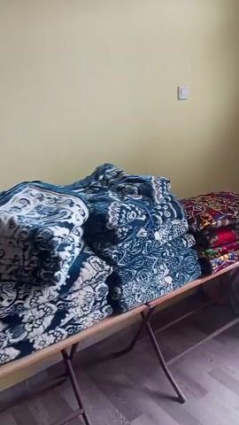 The video shows the interior of a store selling textiles. Stacks of folded bed linens and pillowcases are displayed on shelves and a table. The textiles come in a variety of colors and patterns, including blue, white, red, and burgundy. The shelves are made of metal and the walls are painted a light yellow color. There are no people visible in the video. The camera pans across the merchandise.