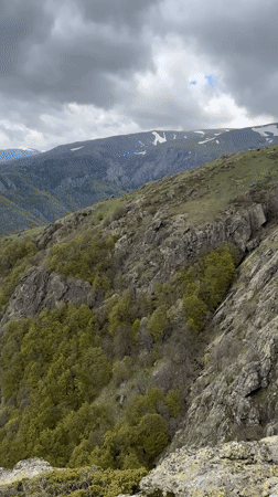 Hikers traverse rocky Bulgarian mountain terrain with waterfall, overcast conditions
