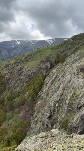 Hikers traverse rocky Bulgarian mountain terrain with waterfall, overcast conditions