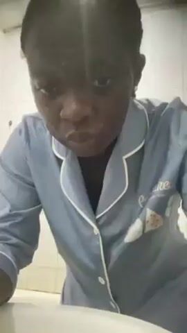 A woman is washing her face in front of a bathroom sink. She has soap on her face and is rinsing it off. She is wearing a light blue pajama top with the word "Cupcake" on the chest. The bathroom has white tiled walls.