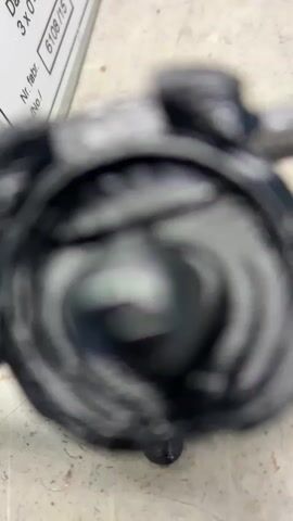 This is a close-up video of a black, 3D-printed figurine resembling a robotic character. The figurine has a circular backpack with protruding shoulder pieces, a helmeted head with a visor, and articulated limbs. It stands on two feet, with its arms bent at the elbows and hands on its hips, giving it a somewhat defiant stance. The figurine is placed on a textured, light-colored surface that appears to be a workbench or a similar utilitarian area.

In the background, a metal panel with printed text is visible. The text is partially obscured and out of focus, but some elements are discernible. One section reads "Dane wyjść" (Output data) followed by "3 x 400 V 60-80A" which suggests technical specifications related to power output. Another label states "Nr. fabr." (Factory number) and "No.t". A "CE" marking is also visible on the panel, indicating compliance with European standards. Further in the background, other objects are present, including what appears to be a red tool with yellow accents and a green component, possibly part of electronic equipment.

The scene appears to be indoors, likely in a workshop or laboratory setting, given the presence of tools and technical equipment. The lighting is somewhat harsh, casting shadows and highlighting the texture of the figurine and the surface it stands on. There is no indication of time of day or weather conditions. The overall impression is one of a technical or hobbyist environment where 3D printing or model making might be taking place. The figurine itself is the primary subject, and its detailed design suggests it might be a character from a video game or a science fiction franchise.