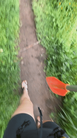 Person with kayak paddle walks muddy trail in Payangan