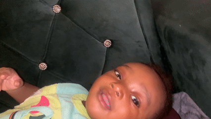 Baby smiles on green couch in Barakin Akawo, Nigeria