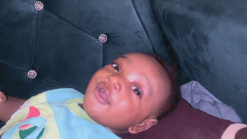 Baby smiles on green couch in Barakin Akawo, Nigeria