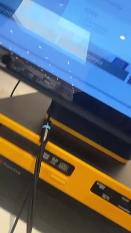 The video shows a close-up, tilted view of a touchscreen display and a yellow device. The touchscreen appears to be in a retail or service environment, displaying text in a blue interface. Some of the visible text includes "Smartphone erkennt" which translates to "Smartphone recognized". There are also bullet points listed under this heading, though they are not fully legible. A red button is partially visible on the right side of the screen. Below the touchscreen, a yellow device with black accents is prominent. A black cable is connected to the yellow device and extends downwards. The lighting suggests an indoor setting, possibly a store or office. The camera movement is somewhat shaky and blurred, indicating it was likely handheld.