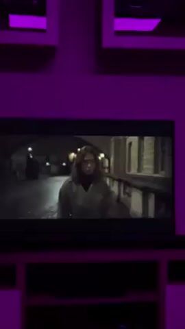 A television screen displays scenes from a movie, set against a backdrop of a room lit with purple light. The screen shows a woman walking along a European city street at night, followed by a shot inside a car with two men driving.
