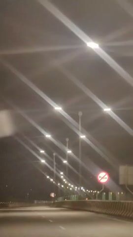 The video shows a highway at night with streetlights illuminating the road. There are no visible vehicles or people. A traffic sign with a red circle and a line through it, indicating "no honking," is visible on the right side of the road. The road appears to be empty, and the scene is dimly lit by the streetlights.