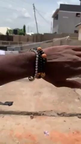 The video shows a person's arm wearing several bracelets. The bracelets are made of different materials, including beads, rhinestones, and what appears to be wood. The person is standing outside in a concrete or tiled area. There are buildings in the background, and laundry is hanging on a clothesline. The sky is overcast. The video focuses on the bracelets.