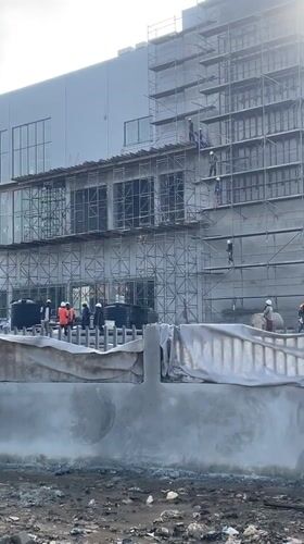 Multi-story construction underway in Abuja with workers and tuk-tuks on site