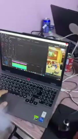 The video shows a person using a laptop in a cluttered environment.  The laptop, a Lenovo model, displays an open video editing program and is emitting white smoke.  The screen then switches to a desktop background with various app icons. The person uses the trackpad. The surrounding area includes a power strip, cans of soda, and other computer peripherals.