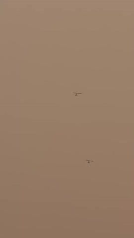 The video depicts two indistinct helicopters in the sky. The background is a hazy, muted brown.