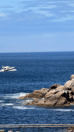 White motorboat cruises past rocky A Coruña coastline