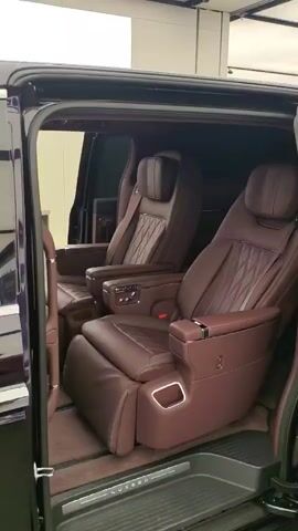 The video displays the interior and exterior of a luxury vehicle. The interior features plush, maroon leather seats with intricate stitching, indicating a high-end finish. The seats appear to be captain's chairs, offering ample legroom and comfort. The exterior showcases a sleek, dark-colored body with chrome accents, including door handles and trim around the windows. The vehicle's front grille and headlights are also visible, featuring modern design elements. The overall impression is one of sophistication and advanced automotive engineering.