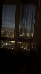 Nighttime city skyline viewed through curtained window