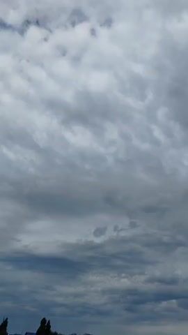The video shows a cloudy sky. At the bottom of the frame, there are trees and some buildings. There is also a wire fence structure visible in the lower right corner of the frame. A male voice can be heard speaking in Russian.
