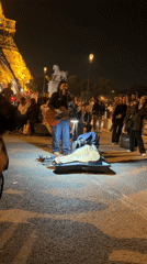 Street musician performs near illuminated Eiffel Tower Friday evening