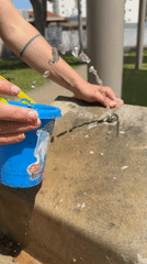 Person fills blue bucket at stone fountain structure