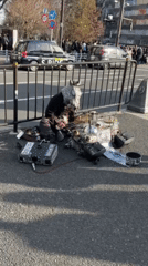 Masked performer with electronics sits on Shibuya sidewalk