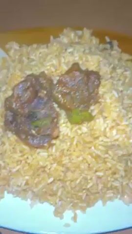 The video shows a plate of rice with beef on top, a plate with a piece of fried chicken, and a portable power station plugged into a wall outlet. The power station is charging. There is music playing in the background. The plates are on a wooden surface. The power station is black and orange.  The charging cable is blue.