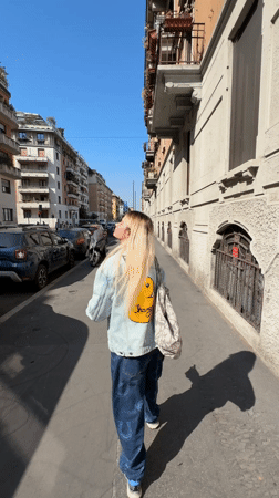 Woman in denim jacket walks sunny Milan sidewalk