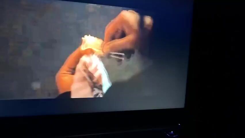 A television screen shows a movie scene of a hand offering a lollipop to a hand holding a small, wrapped package. The scene transitions to a woman holding the lollipop, her face partially visible. "DAN STEVENS" is displayed on the screen. The background appears to be a street scene. The room surrounding the television is dark.