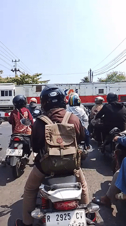 Motorcyclists paused in traffic as a train passes behind