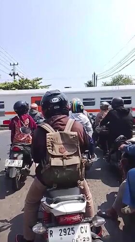 Motorcyclists paused in traffic as a train passes behind