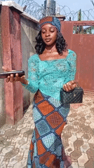 Patterned outfit and headscarf, posing outside a gated courtyard