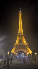 Eiffel Tower glowing at night, crowds gathered on the lawn below