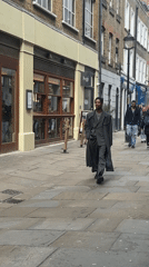 Man in business attire walks London sidewalk with phone