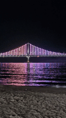 Nighttime crowds gather at Busan beaches viewing illuminated Gwangan Bridge
