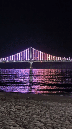 Nighttime crowds gather at Busan beaches viewing illuminated Gwangan Bridge