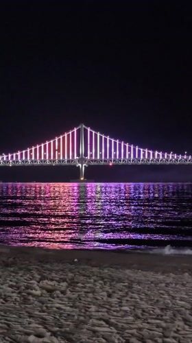 Nighttime crowds gather at Busan beaches viewing illuminated Gwangan Bridge