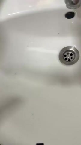 A sink with a faucet and drain is shown. A pink bottle of soap with a strawberry graphic is on the left. A clear green bottle of shower gel with cucumber and aloe vera on the label is brought into view and then placed back down. The pink soap bottle is then picked up and moved.