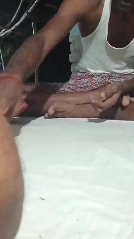 This video captures a close-up view of two individuals engaged in an activity, possibly a card game, in an outdoor setting at night. The primary subject is a person in the foreground, partially visible, with their arm and shoulder in focus. Their skin tone appears to be dark. To their right, another person is seated cross-legged. This individual is wearing a white tank top and patterned shorts. Their hands are actively involved in handling a stack of what appear to be playing cards or currency notes.

The scene is dimly lit, suggesting it is nighttime. The background is dark, with some indistinct shapes that could be foliage or structures. A white sheet or surface covers the ground in front of the seated person, on which some cards or papers have been placed. The overall ambiance suggests a casual gathering or a game being played outdoors in the evening. The focus is on the hands and the objects being manipulated, emphasizing the action of the game. There is no visible text in the video. The location is identified as Kesari, India.