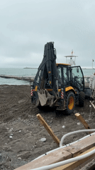 Backhoe operates on Sochi beach near lighthouse and pier
