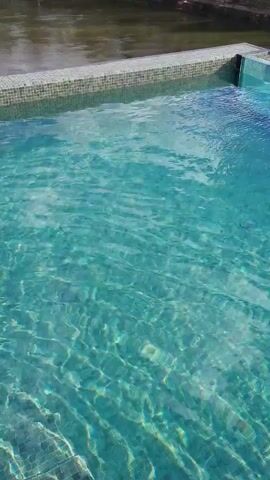 The video shows the view of a person stepping into a pool. The clear turquoise water has a rippled texture. The person’s bare feet are visible stepping down the grey tiled steps of the pool.