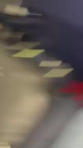The video depicts a close-up of a person's face, specifically their nose and mouth. The person is wearing a blue and white plaid shirt. The background is blurry and dark, with glimpses of another person with brown hair. The audio includes someone saying, "Mila's gonna show us her favorite book on collective memory."