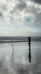 Solitary angler fishes from beach under overcast skies
