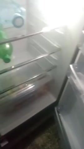 The video shows the inside of a refrigerator. There are two shelves visible. The top shelf has several plastic bottles, mostly blue, some green. The second shelf has a green bottle on it. The refrigerator is brightly lit. The camera moves slightly during the video.