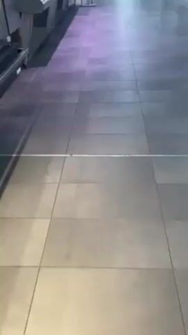 The camera moves across a tiled floor, past a stainless-steel display case on wheels. The tiles are gray and then change to white. The scene ends with a view of a stainless-steel wall and a ventilation duct.