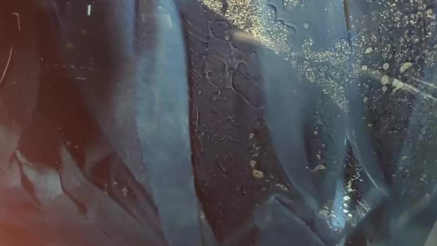 A dashcam is mounted to the interior of a vehicle, showing a blue, textured surface. The camera is angled downwards and to the right. The blue surface appears to be a fabric or carpeted material and has a rough texture with some visible fibers. Light is reflecting off the surface, creating highlights and shadows. The camera's screen is visible and displays a bright, blue image. The overall scene is dark, with the primary light source appearing to be from the camera itself and the screen.