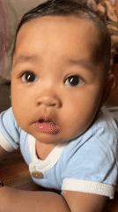 Baby in blue onesie looks up at the camera in Kruengmate